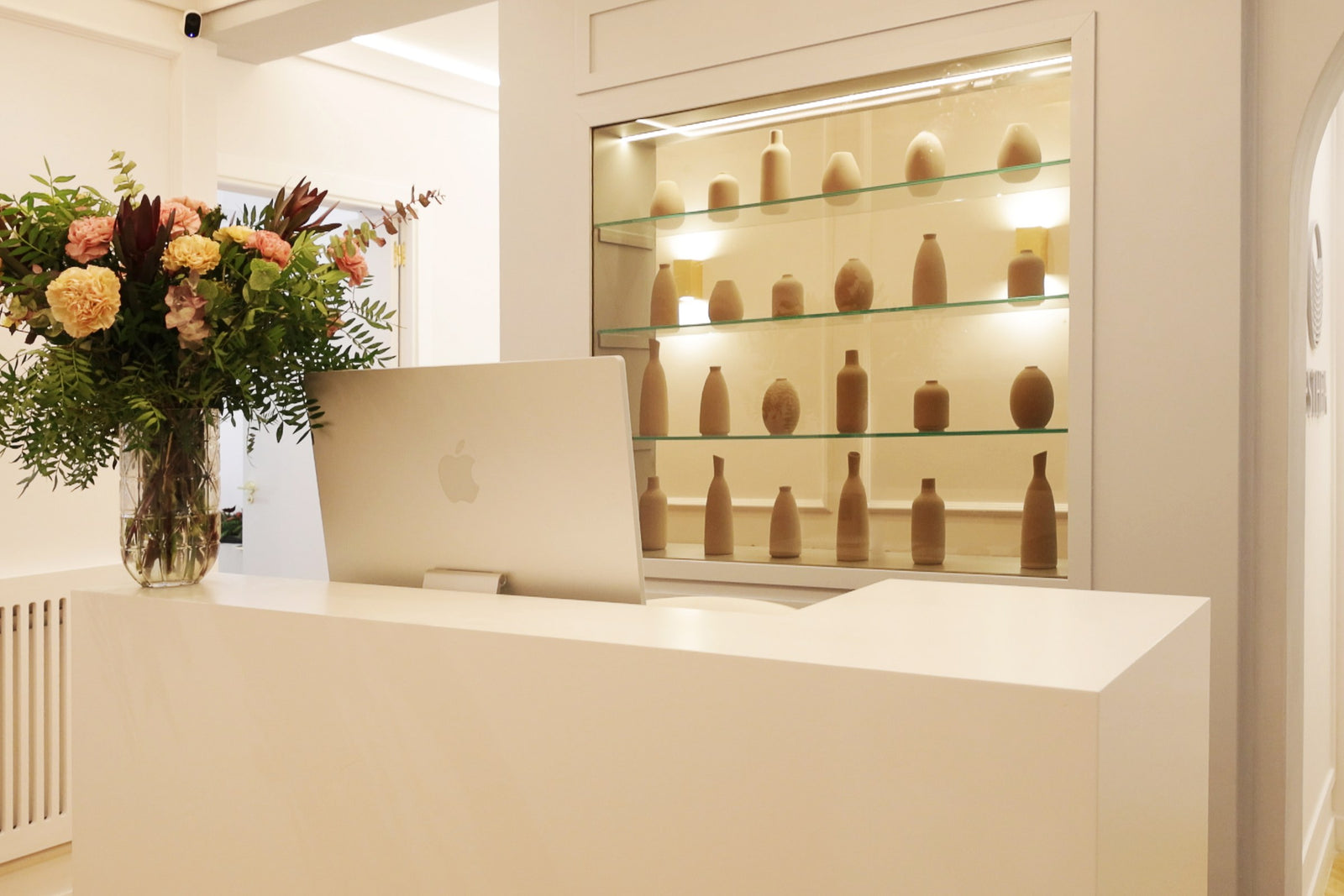 Recepción de Esthea Medica, con la vitrina iluminada y un ramo de flores sobre el mostrador